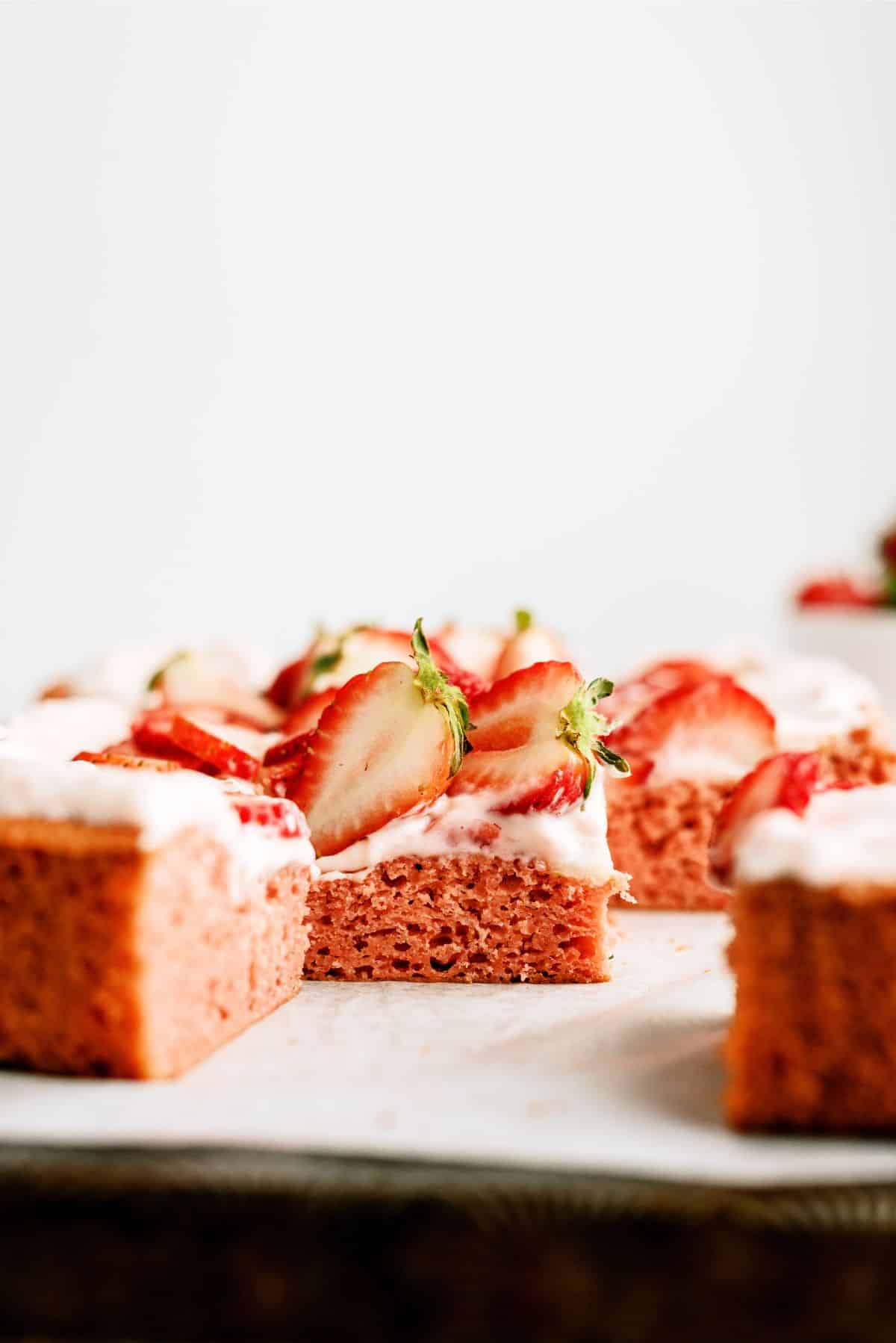 Frosted Strawberry Sheet Cake cut into squares with fresh strawberries on top