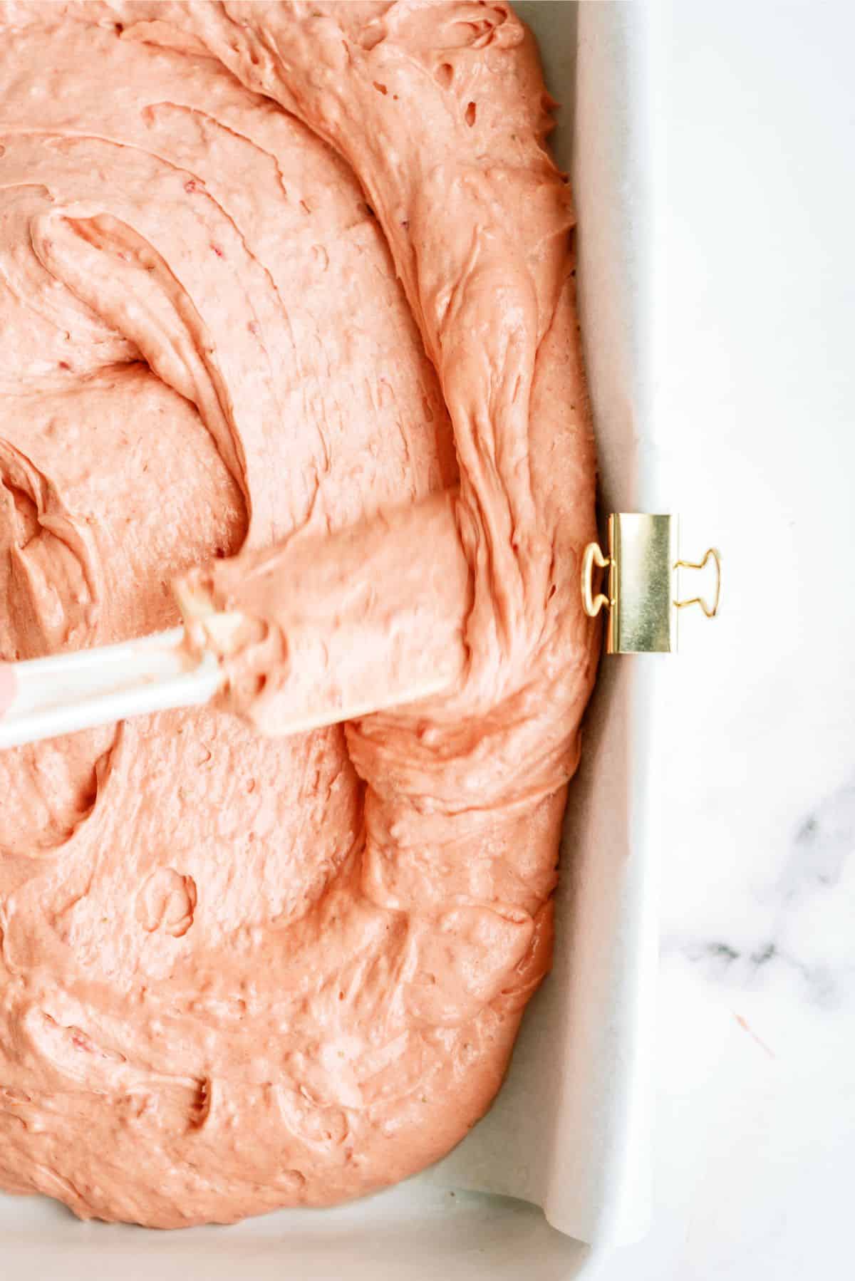 Spreading strawberry cake batter into baking dish with a spatula.