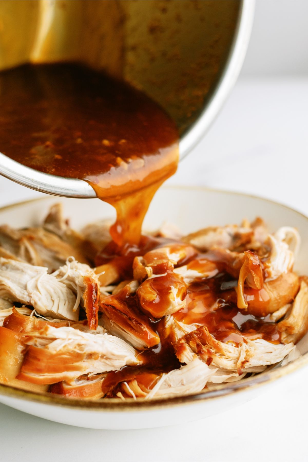 Pouring thickened sauce over shredded chicken