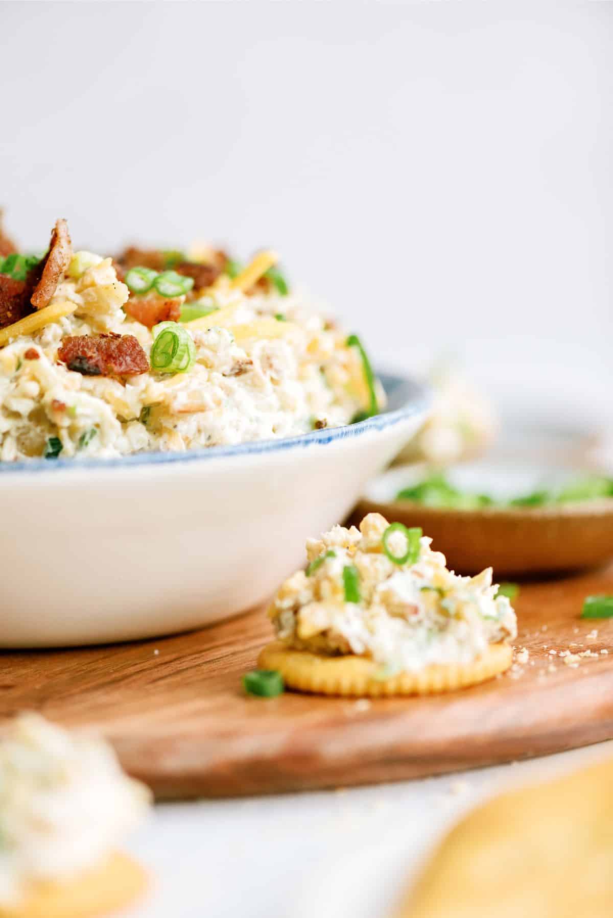 Side view of a bowl of Million Dollar Dip with a cracker topped with dip