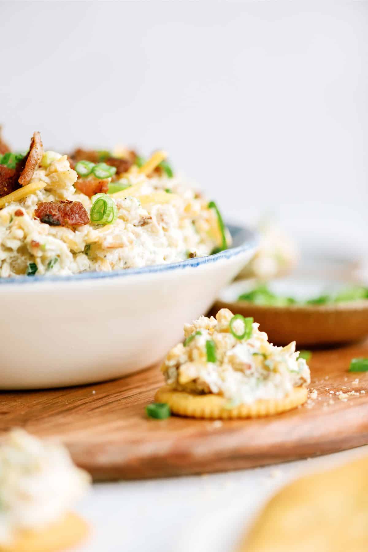 Side view of a bowl of Million Dollar Dip with a cracker topped with dip