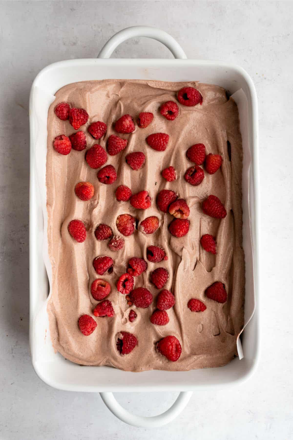 Pudding mixture and fresh raspberries layered over chocolate graham cracker base in baking dish.