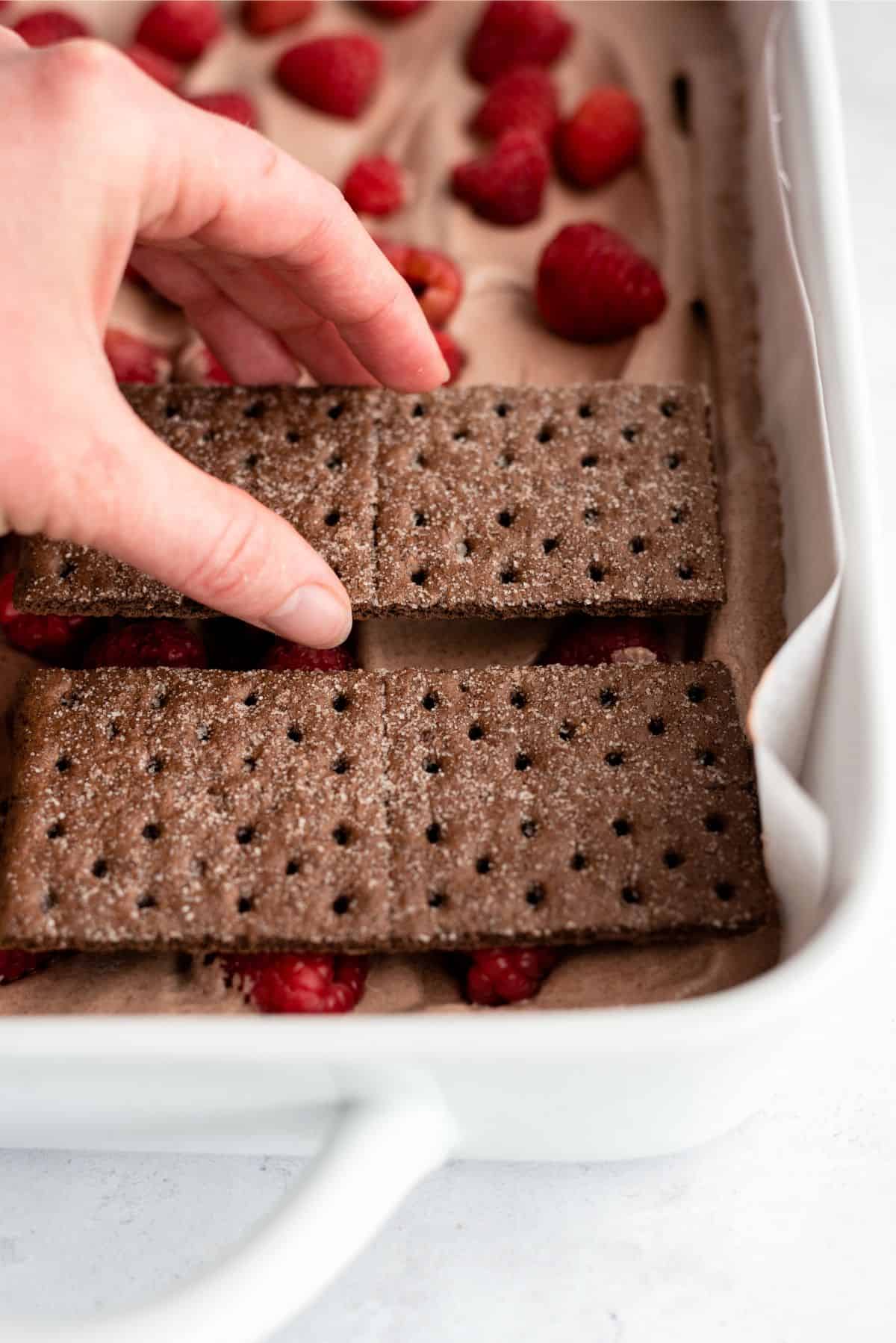 Placing a layer of graham cracker squares on top of the raspberry layer.