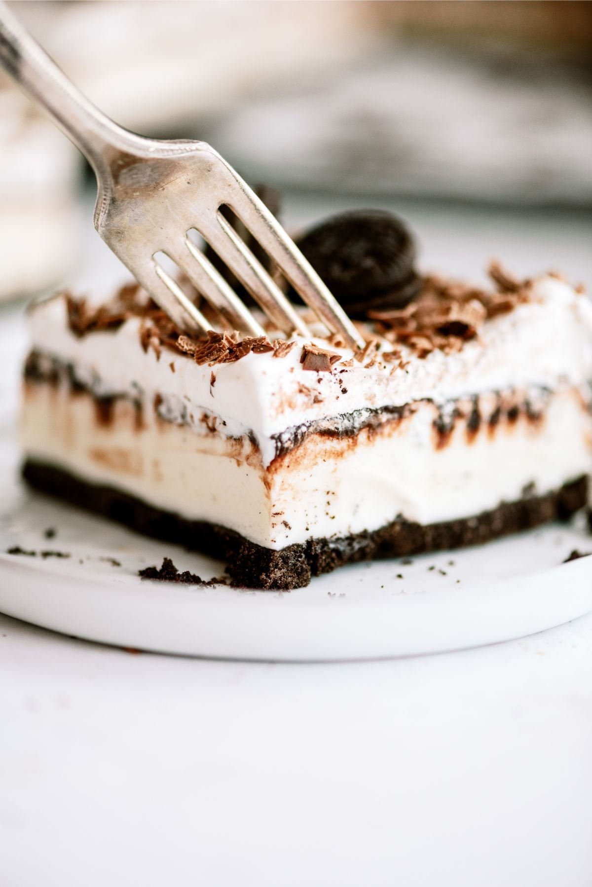 A fork taking a bite out of a slice of  No-Bake Oreo Ice Cream Cake Dessert (Nummy Mess Recipe) on a plate