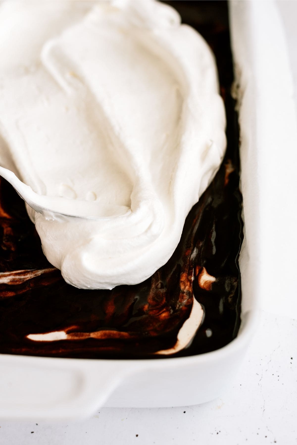 Top layer of whip cream spread over ice cream cake in baking dish.