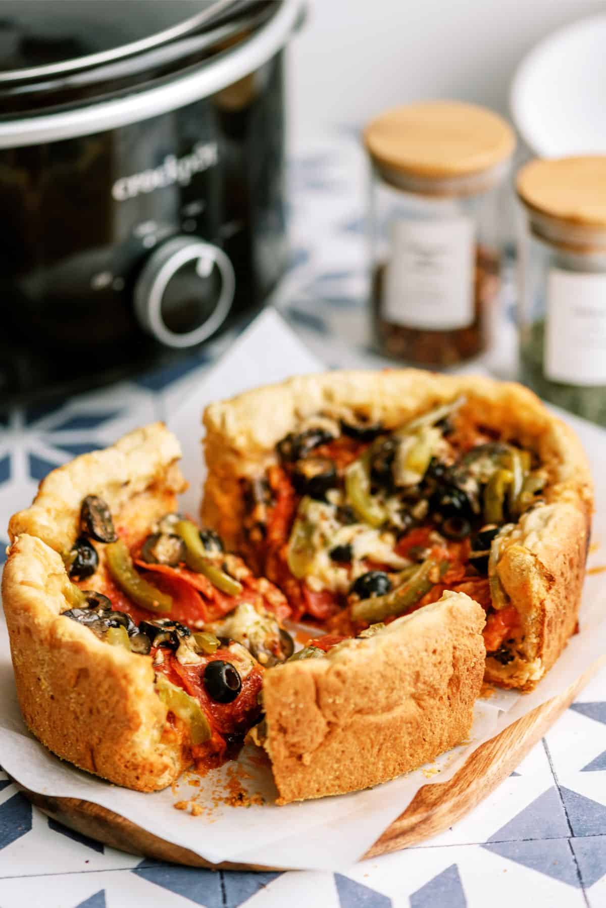 Slow Cooker Deep Dish Pizza on a cutting board with a slow cooker in the background