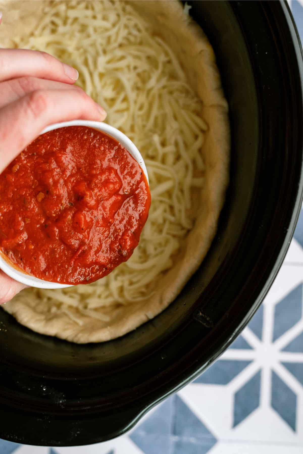 Adding marinara sauce on top of cheese and pizza dough layer