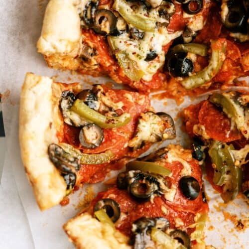 Close-up of a deep-dish pizza topped with tomato sauce, black olives, green peppers, mushrooms, and melted cheese, with one slice partially removed.