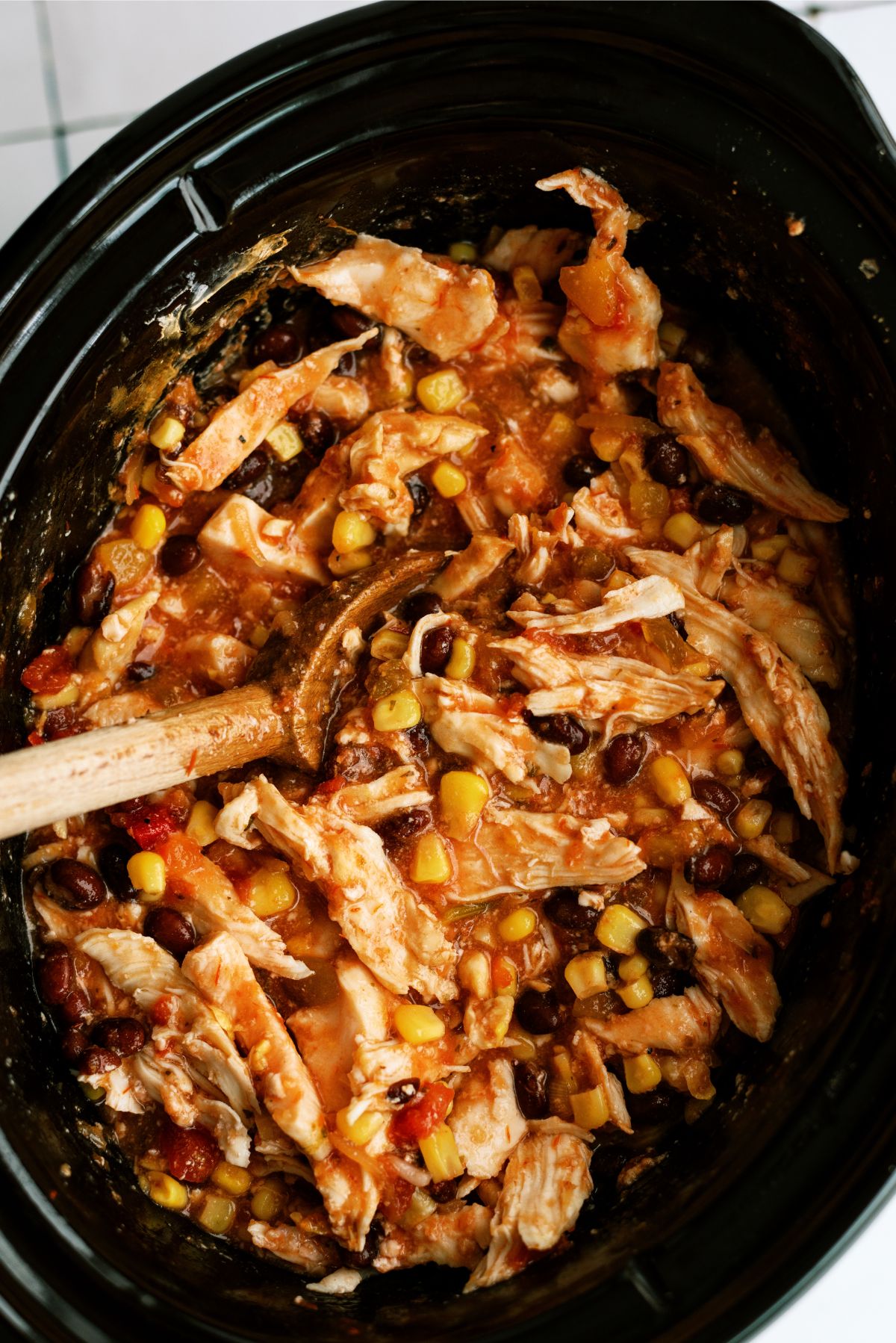 Slow Cooker Mango Chicken in the crock pot with a wooden spoon