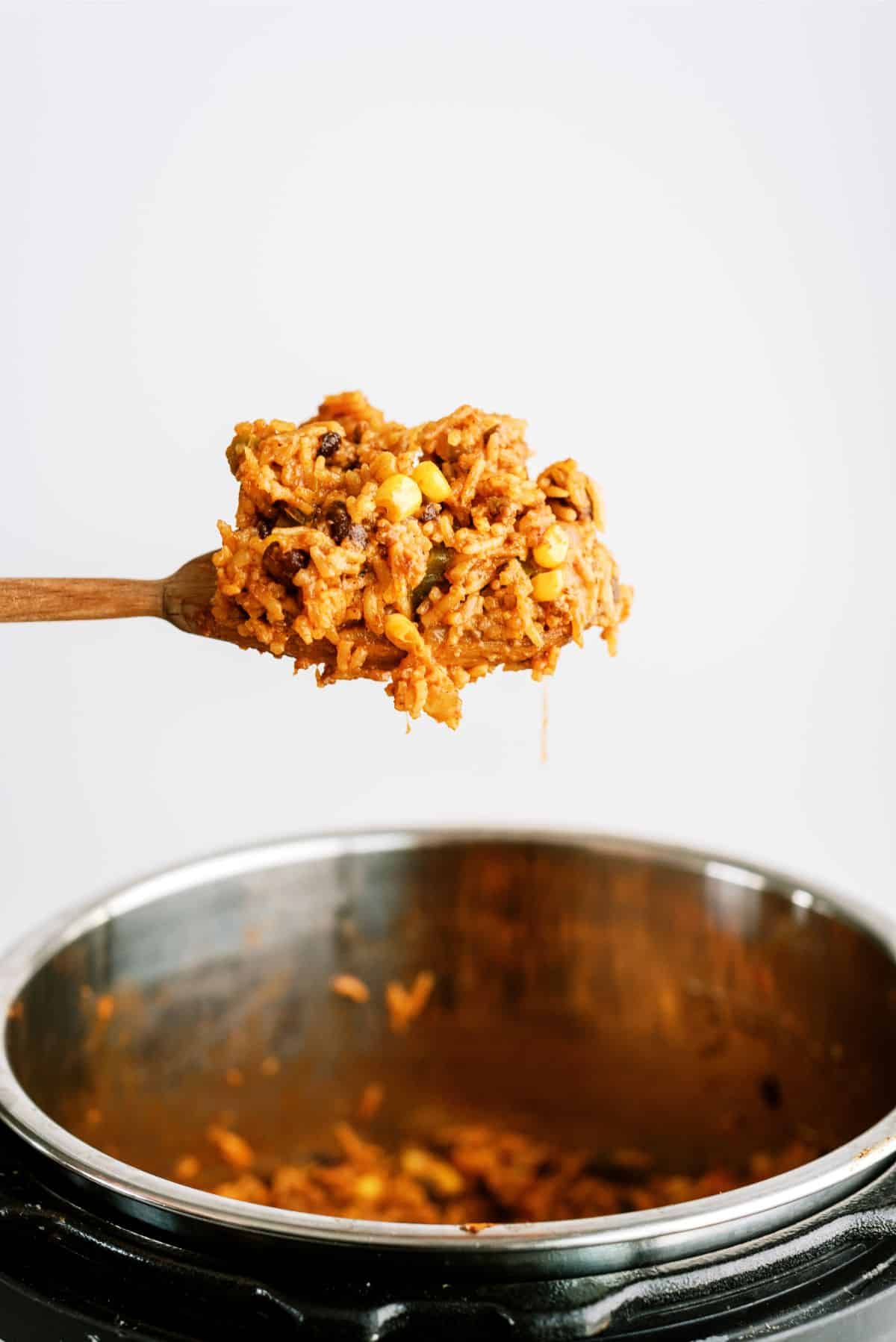 A wooden spoon full of Instant Pot Ground Beef Burrito Bowl mix above an Instant pot