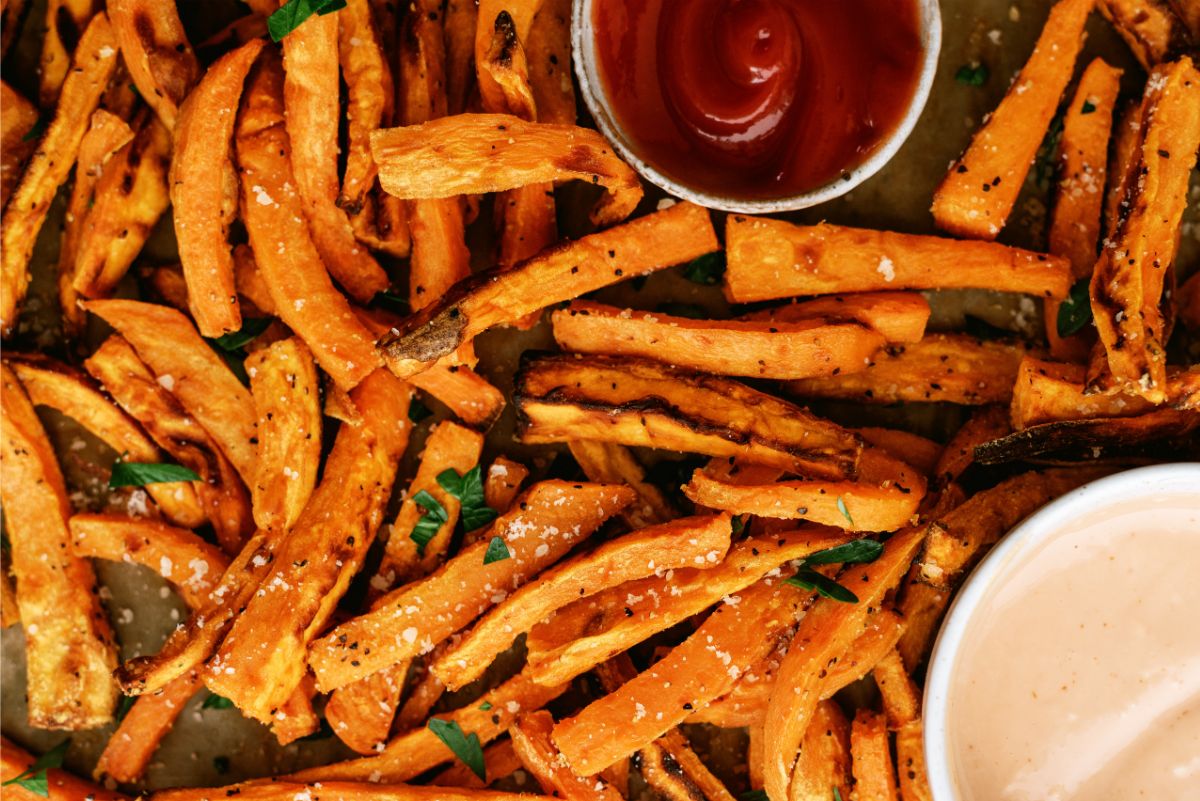 Baked Sweet Potato Fries on a baking sheet with a side of ketchup and fry sauce