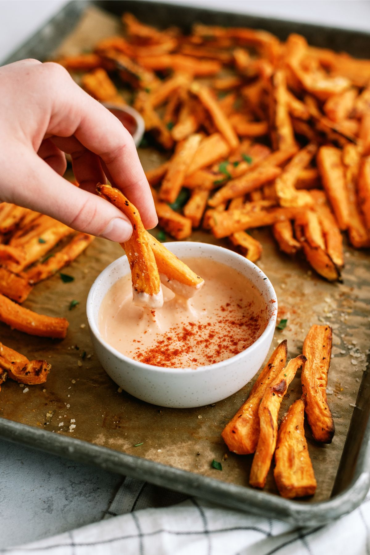 Dipping Baked Sweet Potato Fries in fry sauce with a pan of Baked Sweet Potato Fries in the background