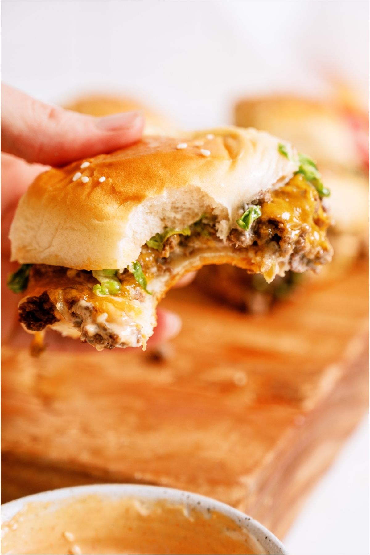 Big Mac Sliders on cutting board with a hand lifting one slider with a bite out of it.