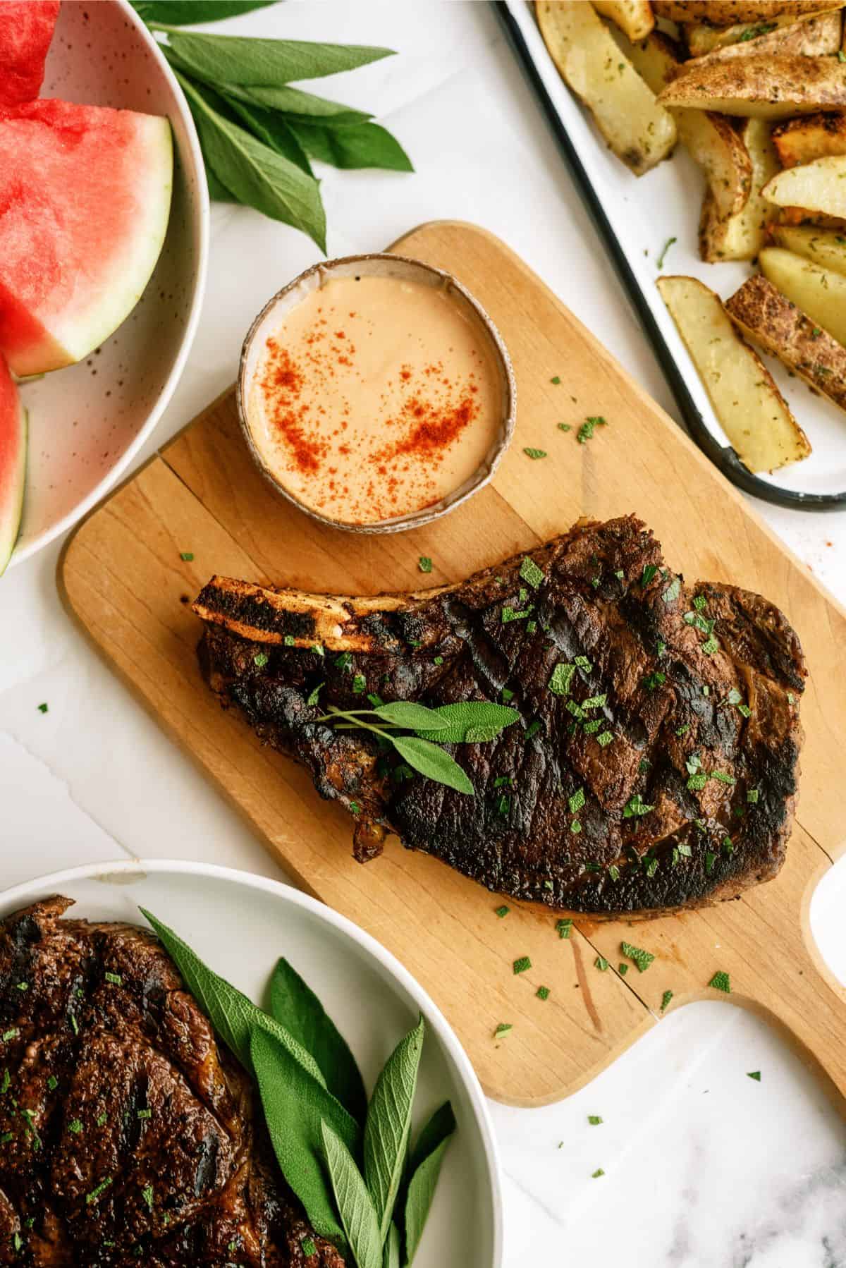 Grilled Ribeye Steak on cutting board with fries and watermelon in the background