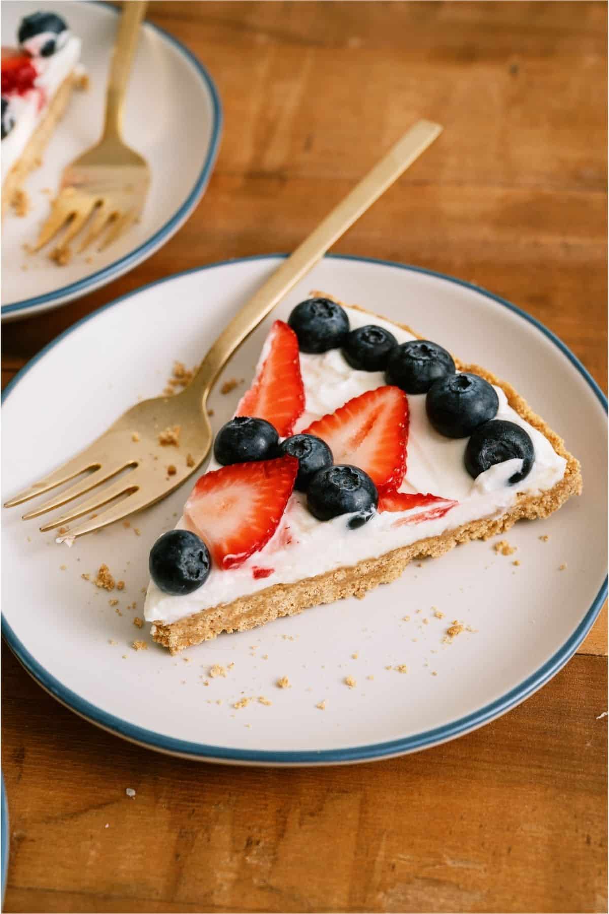 A slice of Patriotic Fruit Pizza on a white plate with a fork.