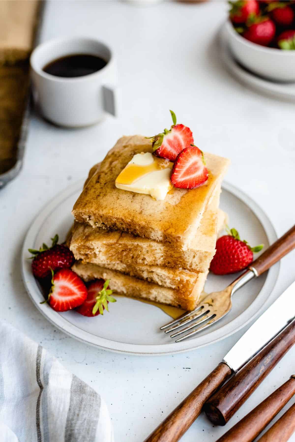 Sheet Pan Pancakes sliced and stacked on a plate with strawberries and syrup