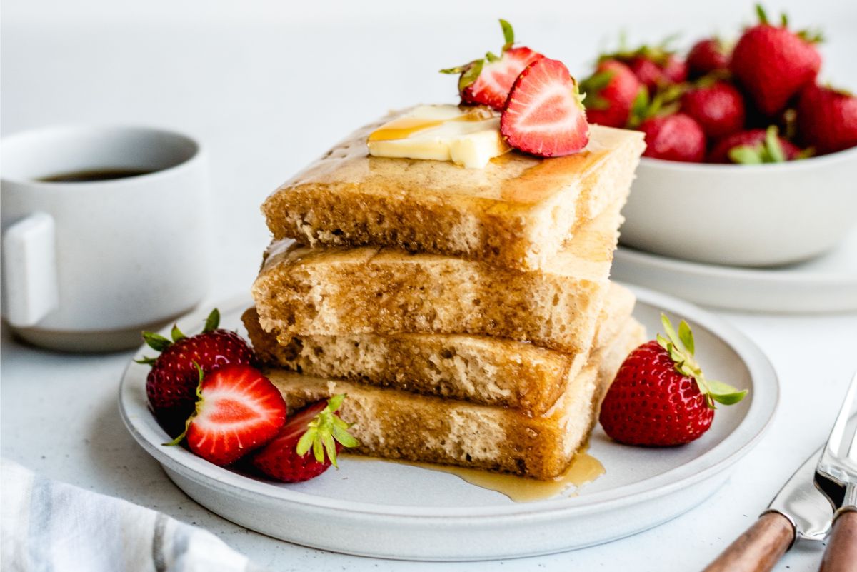 Sheet Pan Pancakes sliced into squares, stacked on a plate with syrup and strawberries