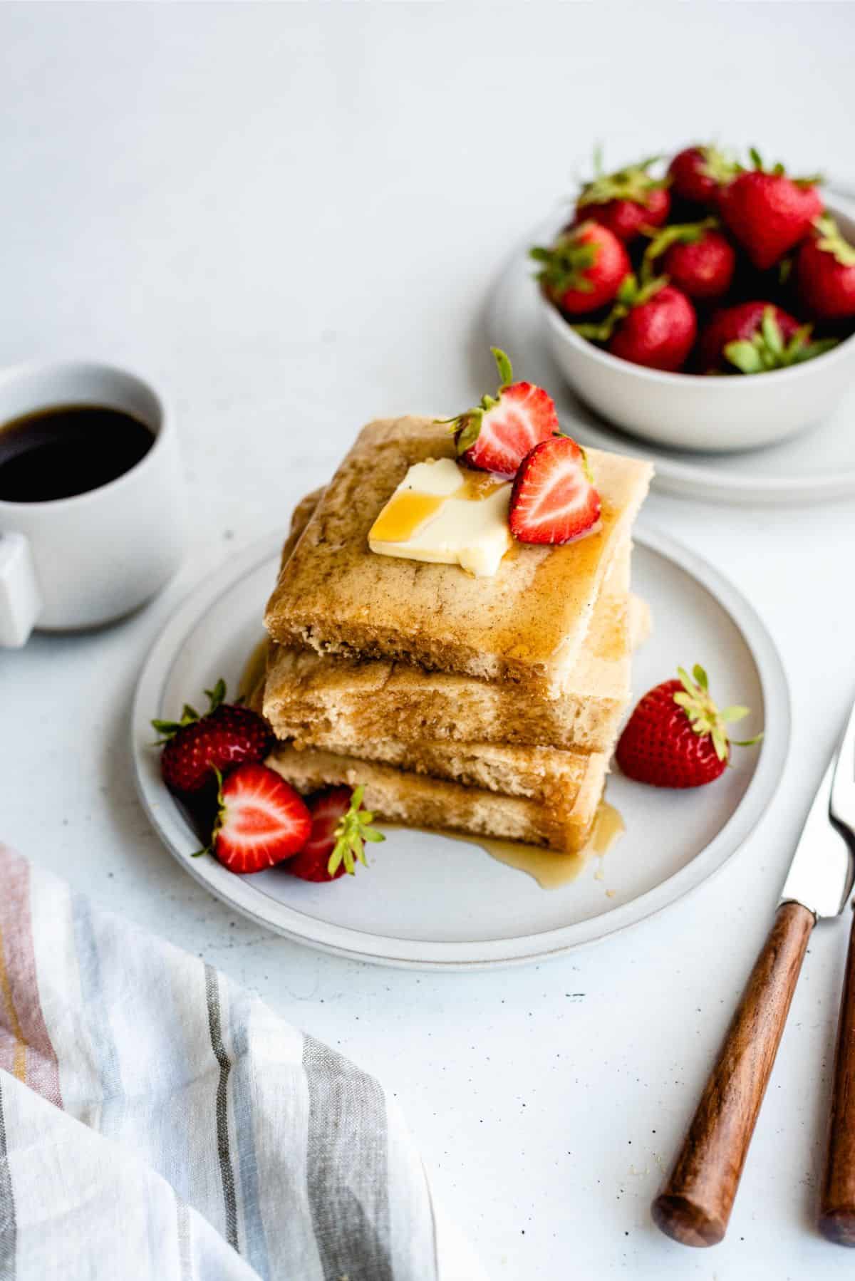 Top view of Sheet Pan Pancakes cut into squares and served on a plate with syrup and strawberris