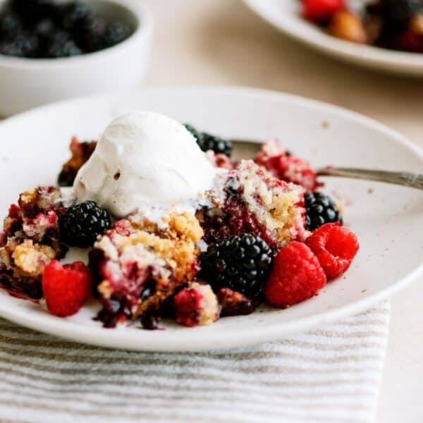 A serving of Slow Cooker Berry Cobbler on a plate with a fork topped with a scoop of ice cream.
