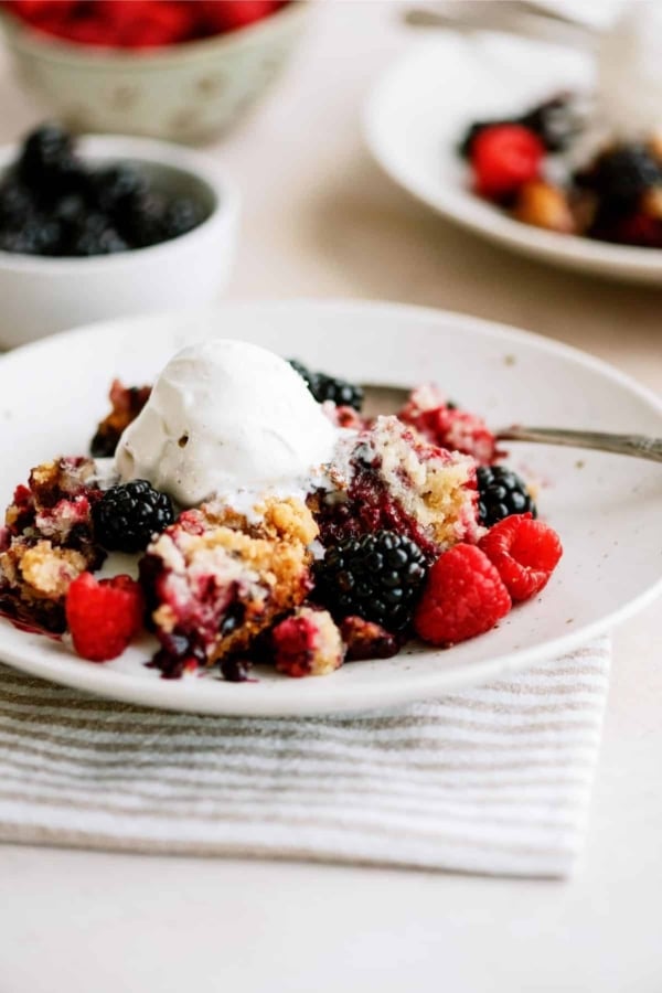 A serving of Slow Cooker Berry Cobbler on a plate with a fork topped with a scoop of ice cream.