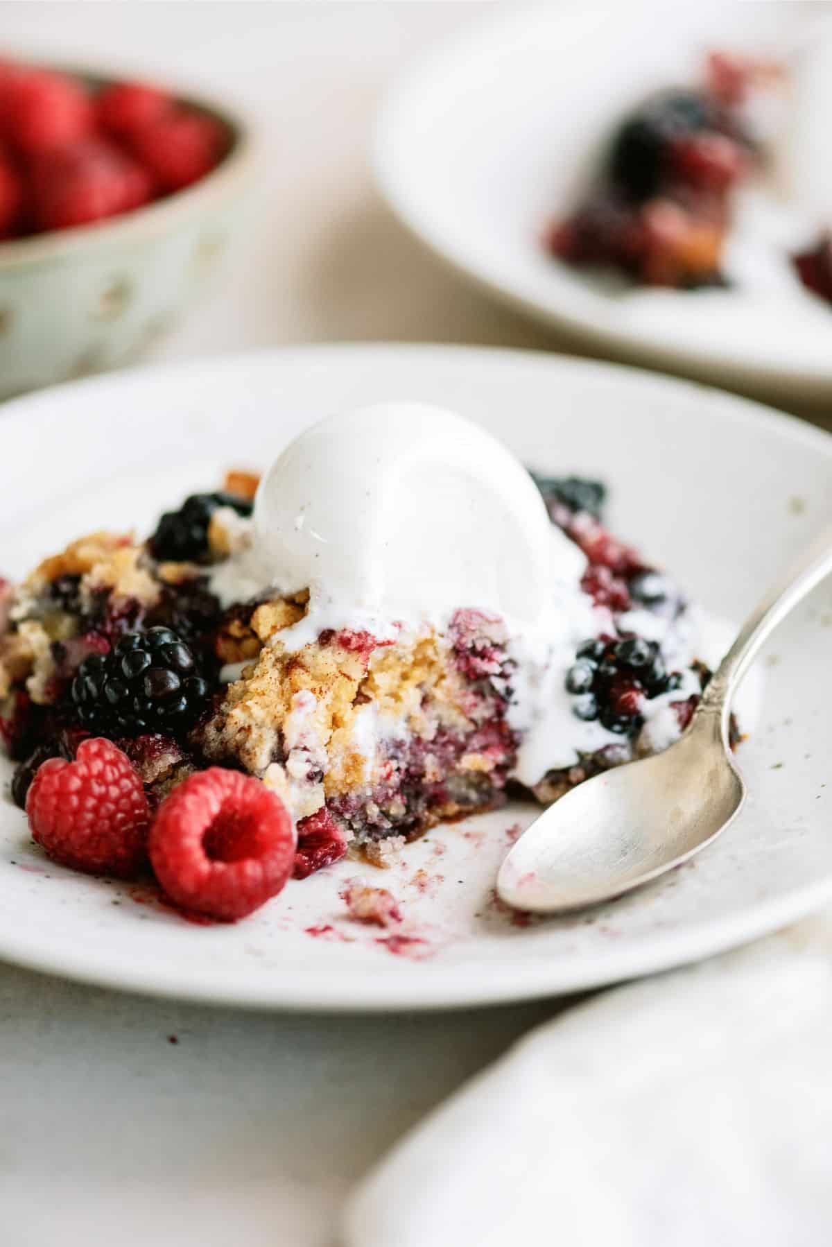 A serving of Slow Cooker Berry Cobbler topped with ice cream on a plate with a spoon.