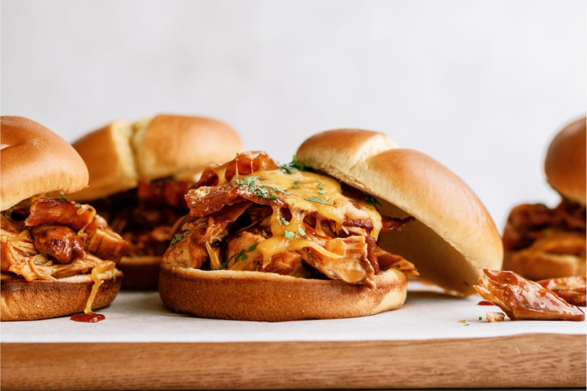 Side view of Slow Cooker Cheesy BBQ Chicken Bacon Sandwiches on a cutting board