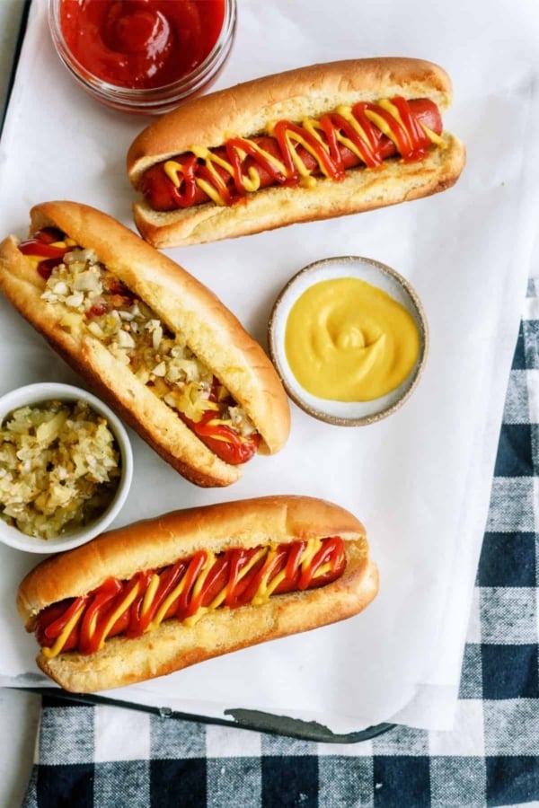 Three hot dogs with mustard and ketchup on a white tray.