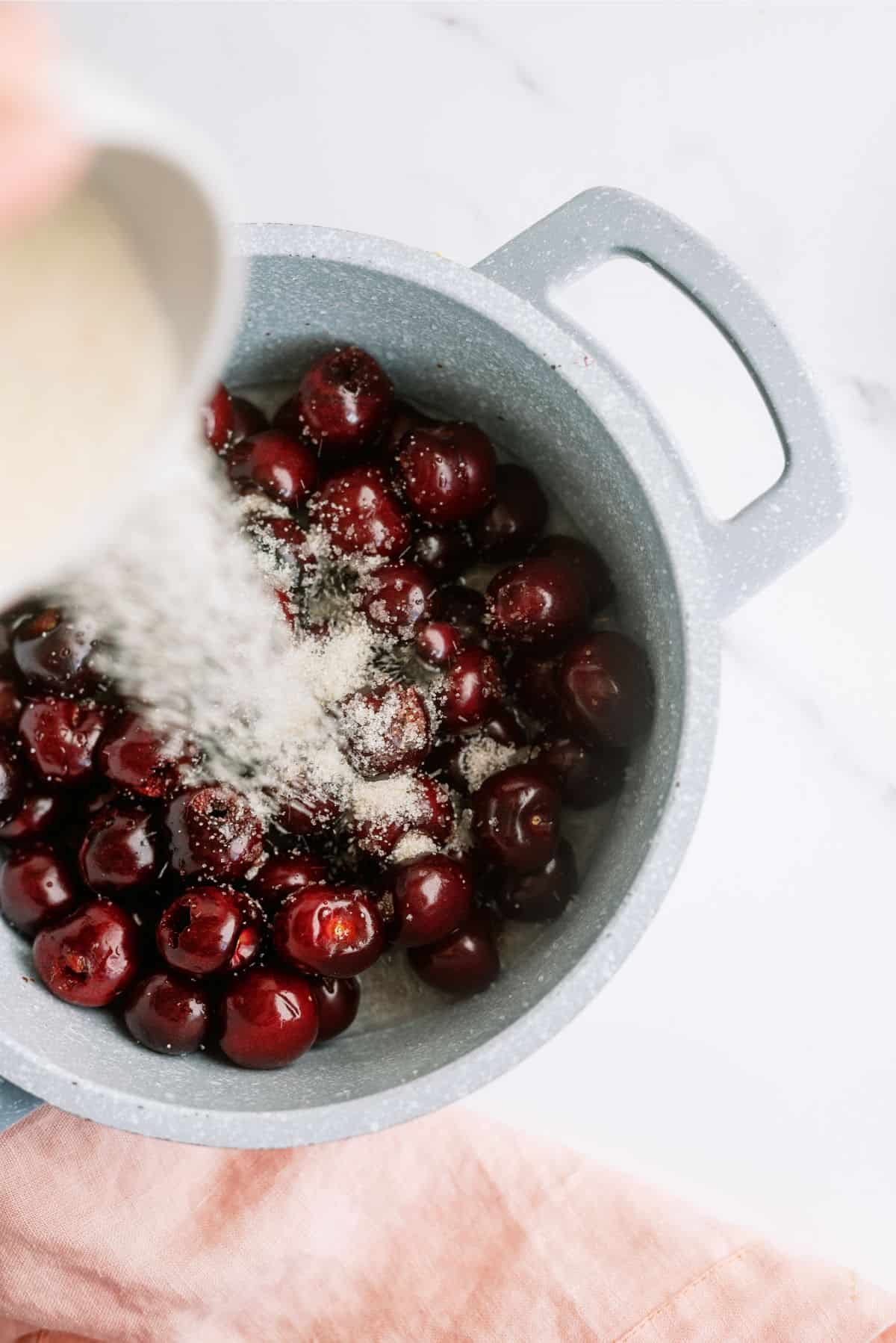 Cherries in a saucepan with cornstarch being sprinkled on top.