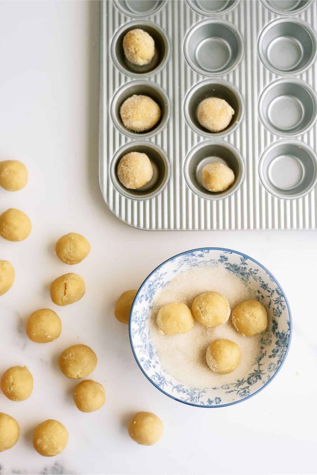 Sugar cookie dough balls. Some in muffin tin and some dough balls rolled in a sugar mixture.