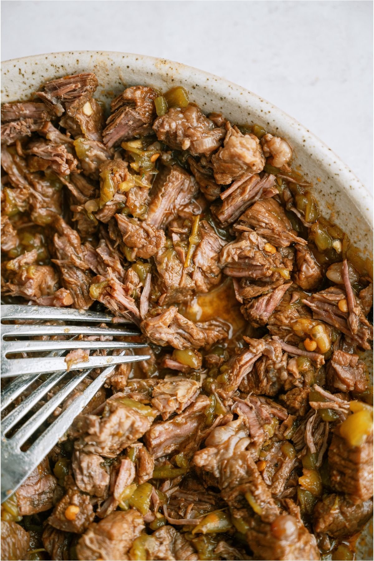 Shredding Copycat Chipotle Barbacoa on a plate with two forks.