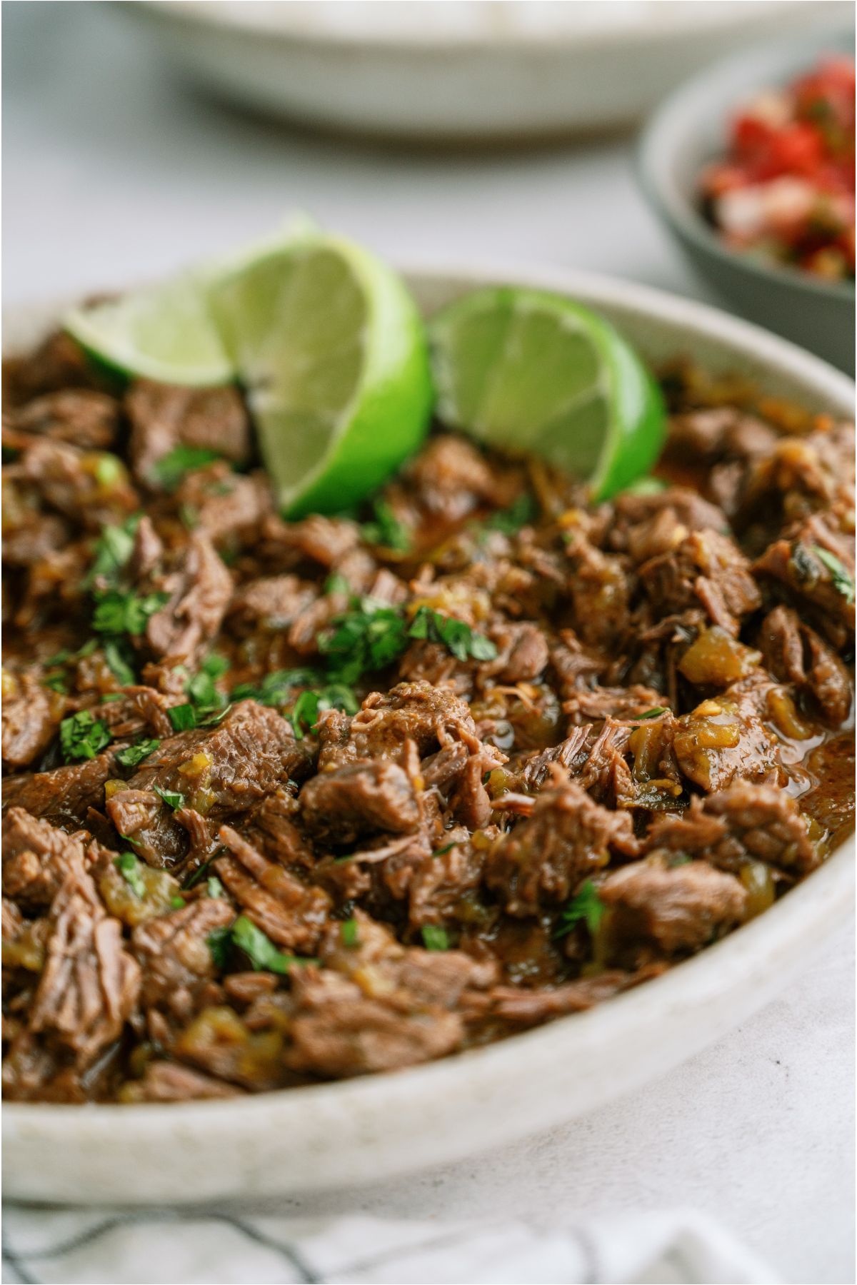 A serving bowl of Copycat Chipotle Barbacoa topped with 3 lime wedges.
