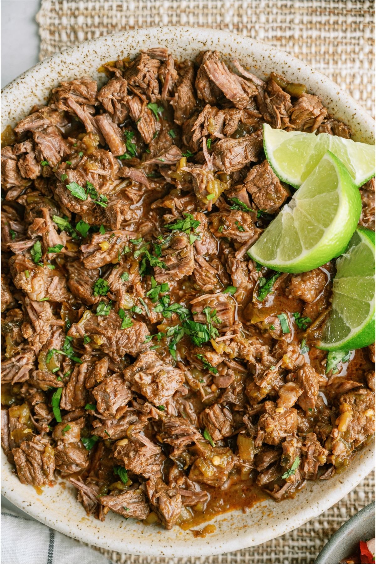 Close up top view of a bowl of Copycat Chipotle Barbacoa topped with 3 lime wedges.