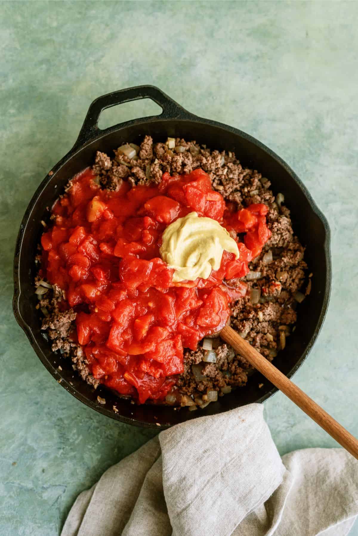 Tomatoes and mustard added to cooked meat in skillet