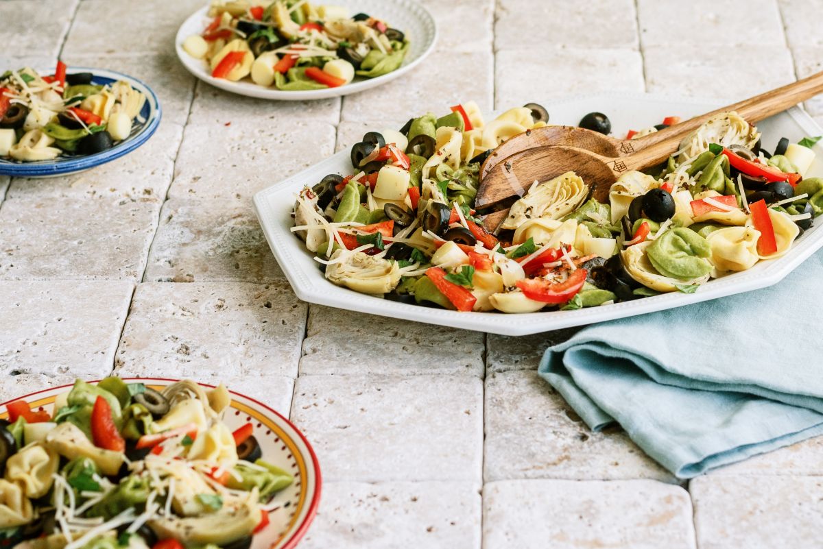 Large serving dish with Italian Tortellini Salad and 3 plates with servings of Italian Tortellini Salad on them
