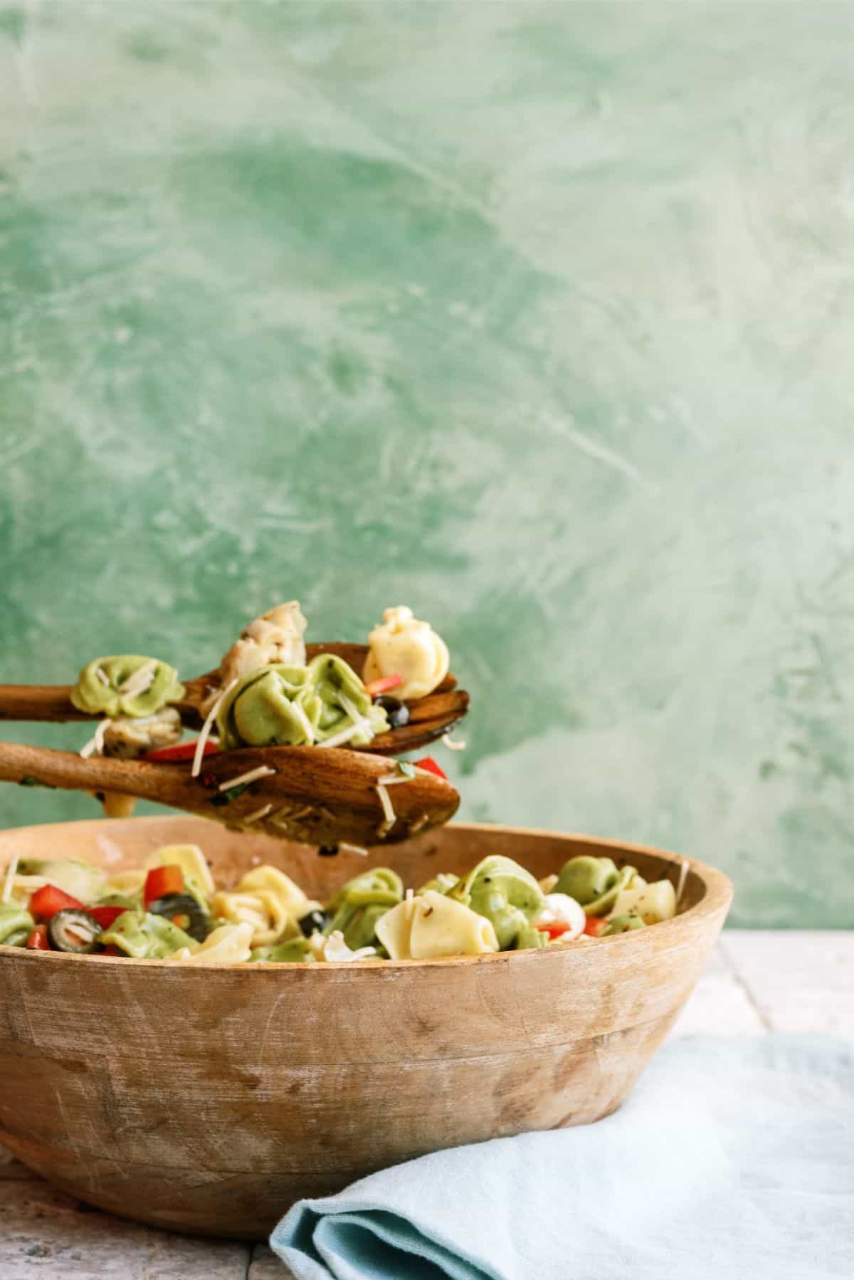 Serving spoons holding a small amount of Italian Tortellini Salad over a bowl filled with Italian Tortellini Salad