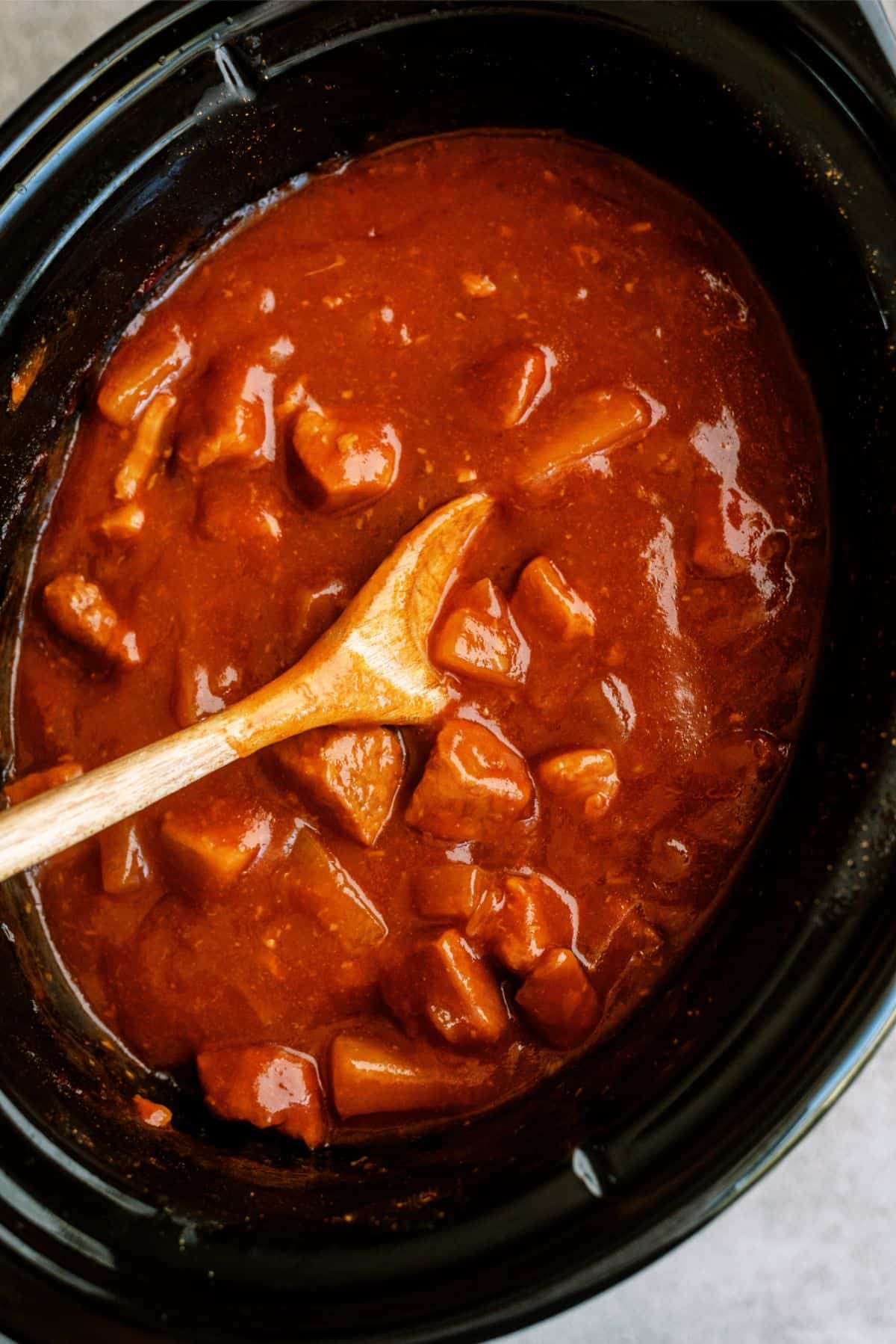 Slow Cooker Sweet and Tangy Pork in the slow cooker with a wooden spoon