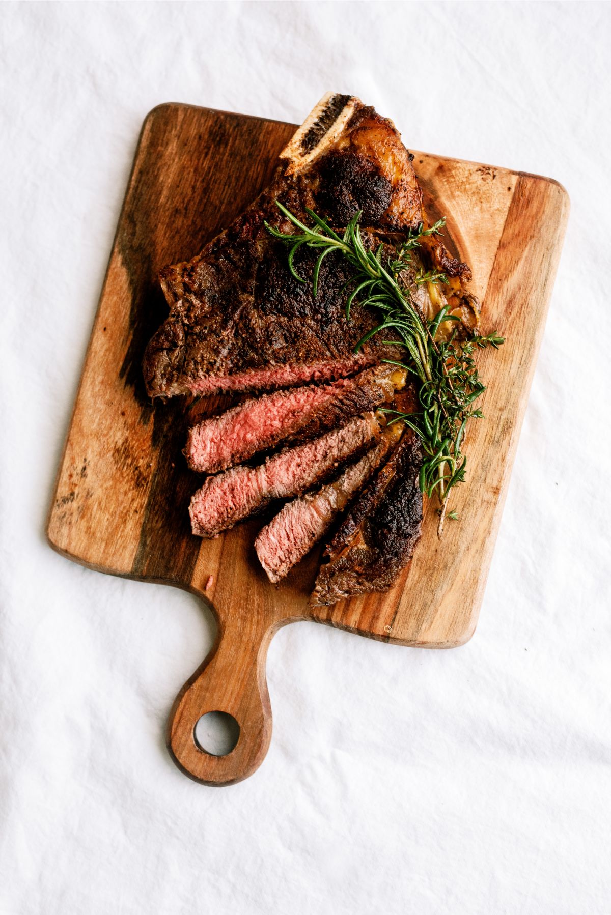 Bone New York Strip Steak grilled and sliced on a cutting board