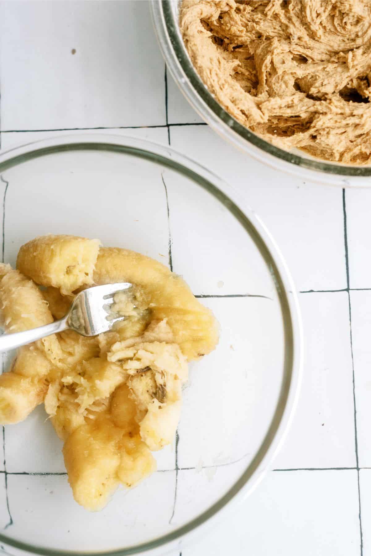 Mashing bananas with a fork in a medium mixing bowl