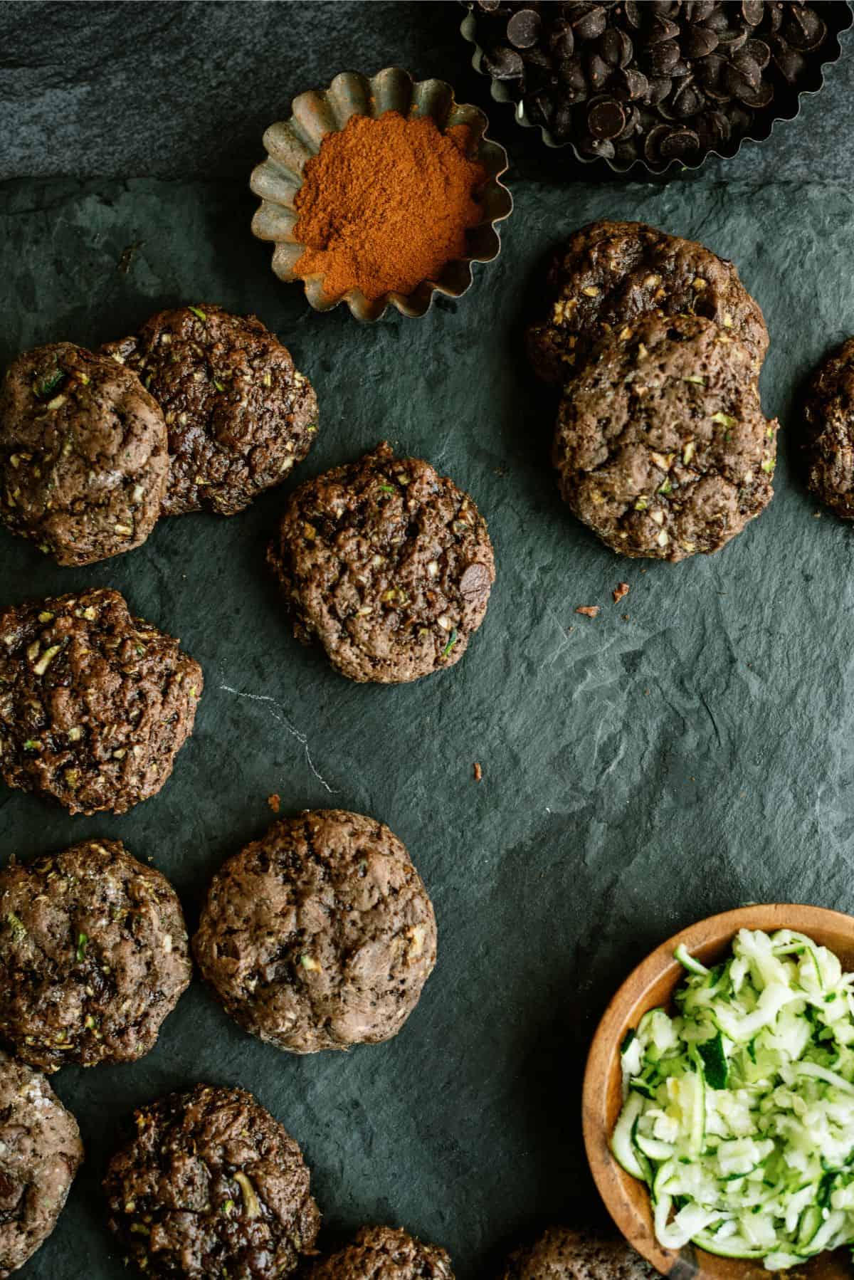 Double Chocolate Zucchini Cookies with a small bowl of zucchini and a small bowl of cinnamon.
