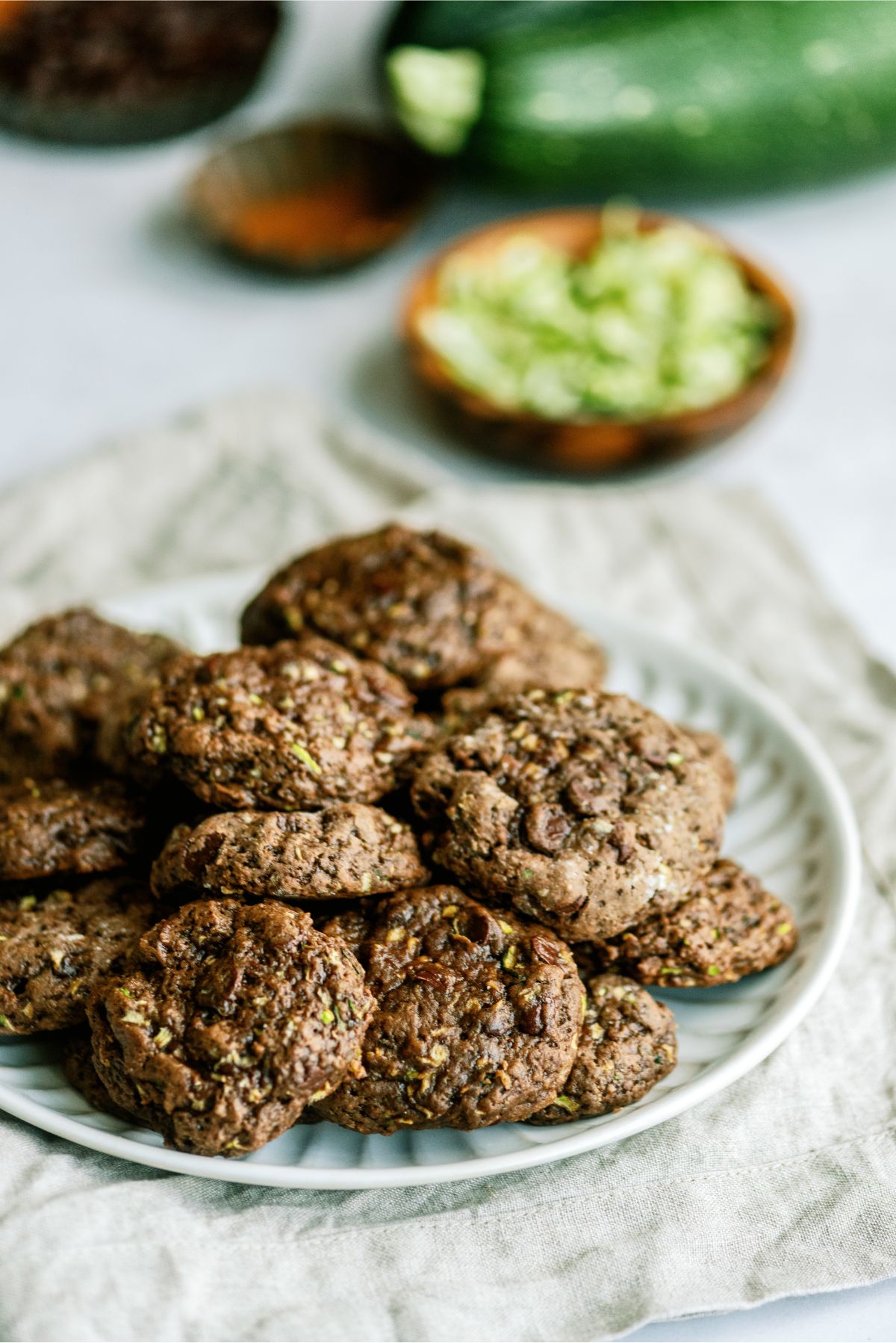 Double Chocolate Zucchini Cookies on a plate with zucchini and cinnamon in the background