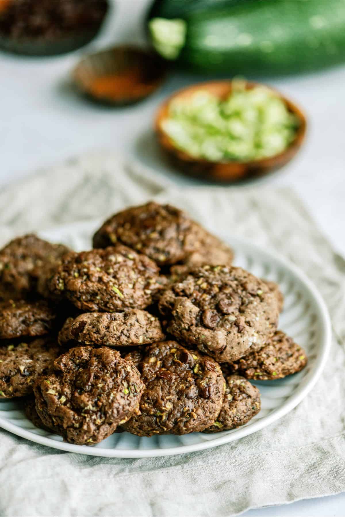 Double Chocolate Zucchini Cookies on a plate with zucchini and cinnamon in the background.