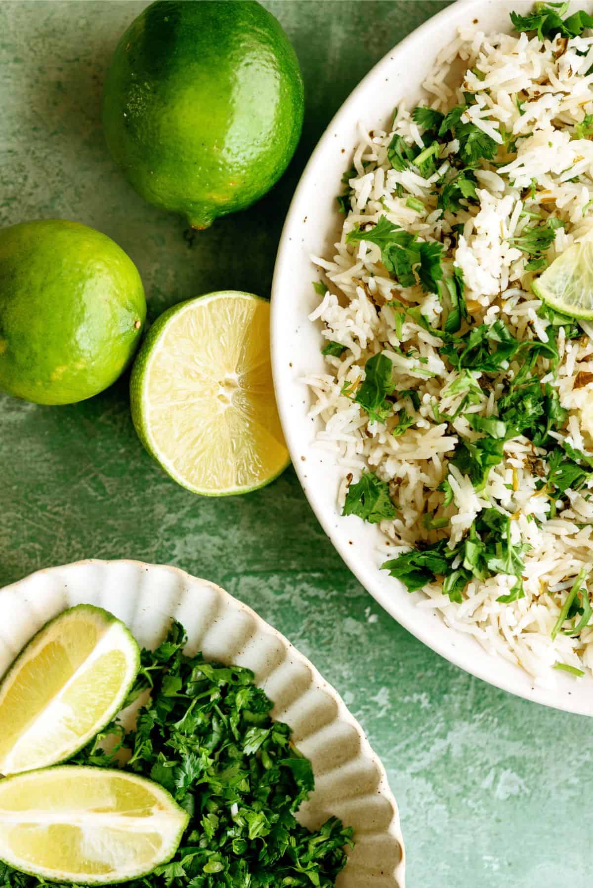 A plate of Instant Pot Cilantro Lime Rice with a plate of Chopped cilantro, surrounded by limes