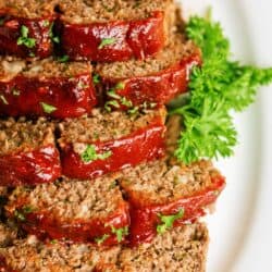 Delicious meatloaf slices topped with ketchup and fresh parsley on a white plate.