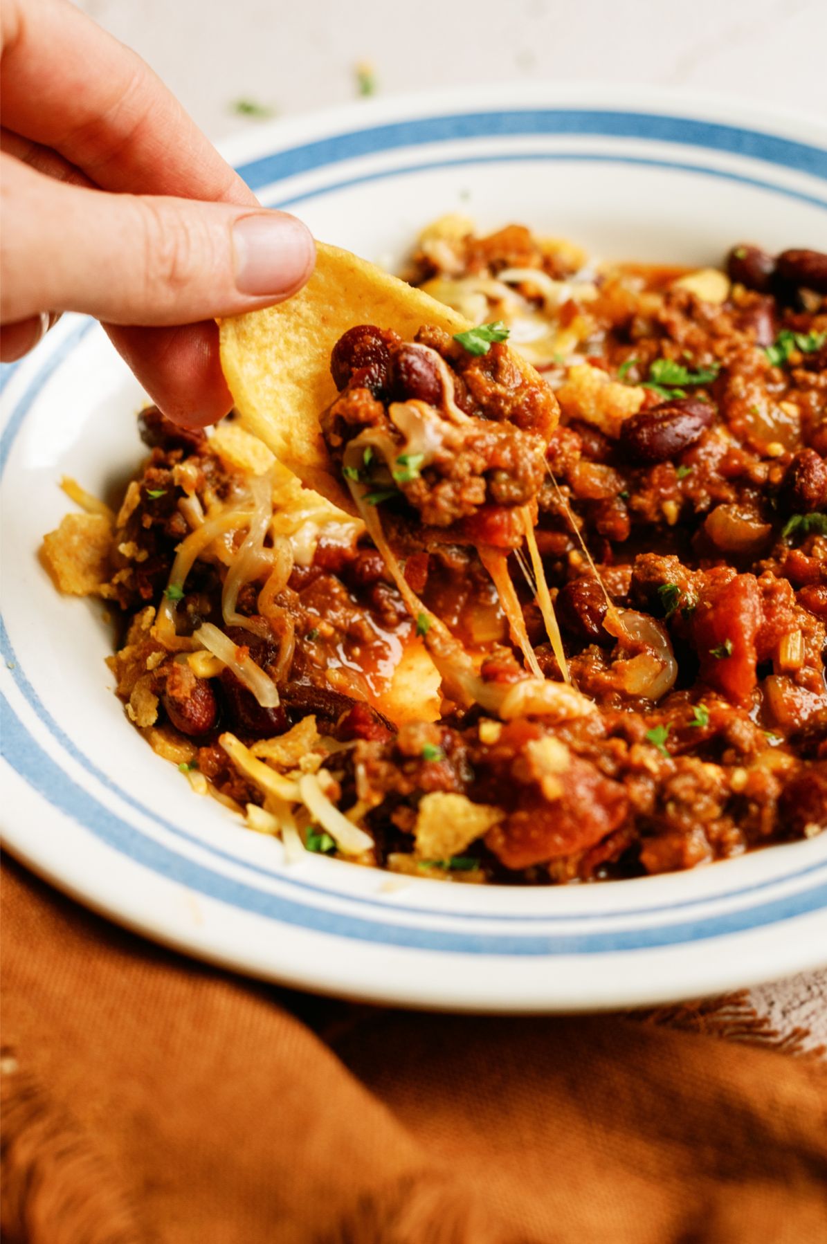 A bowl of Mom's Slow Cooker Chili with a corn chip scooping out a bite