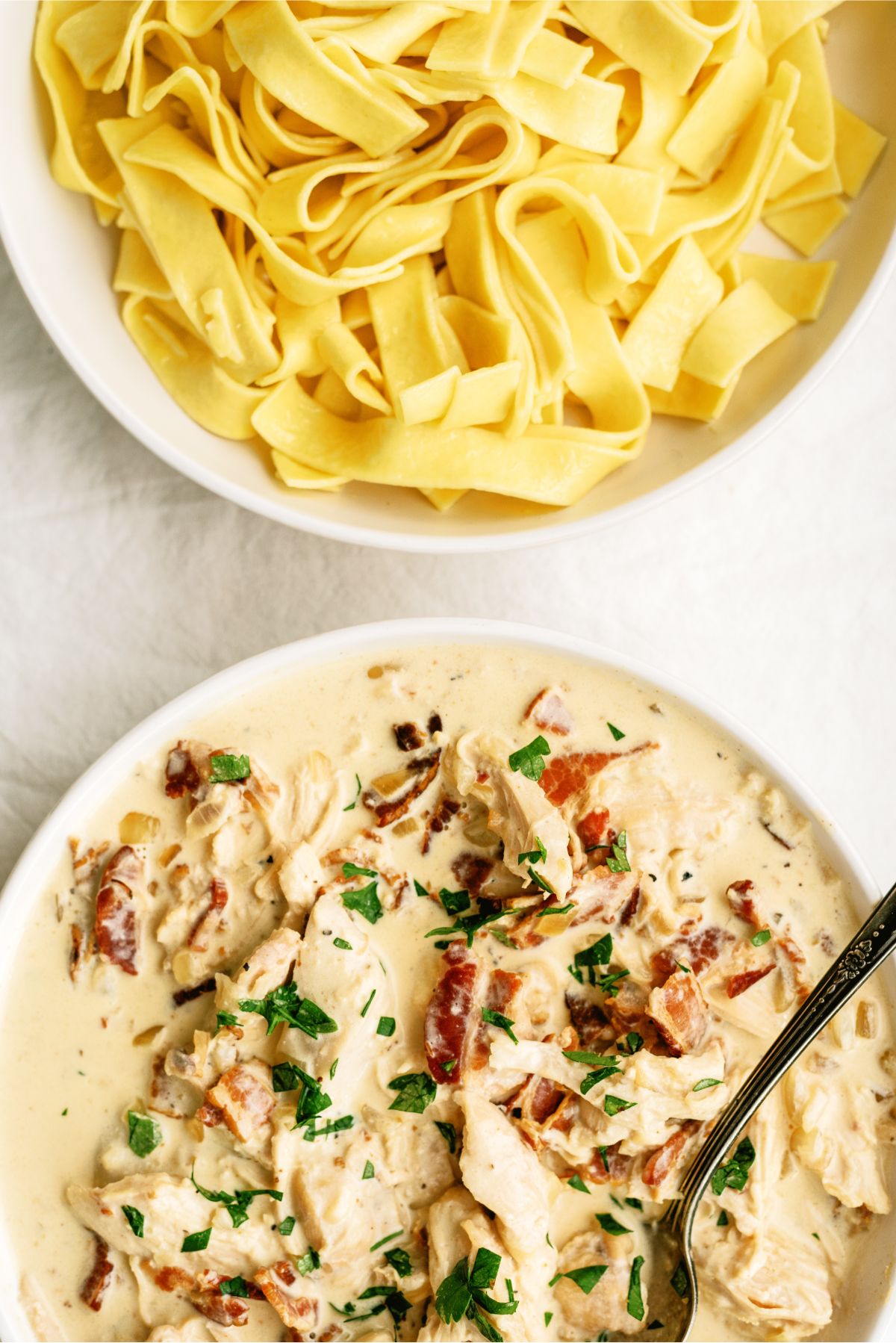 A bowl of Slow Cooker Creamy Bacon Chicken and a bowl of cooked egg noodles