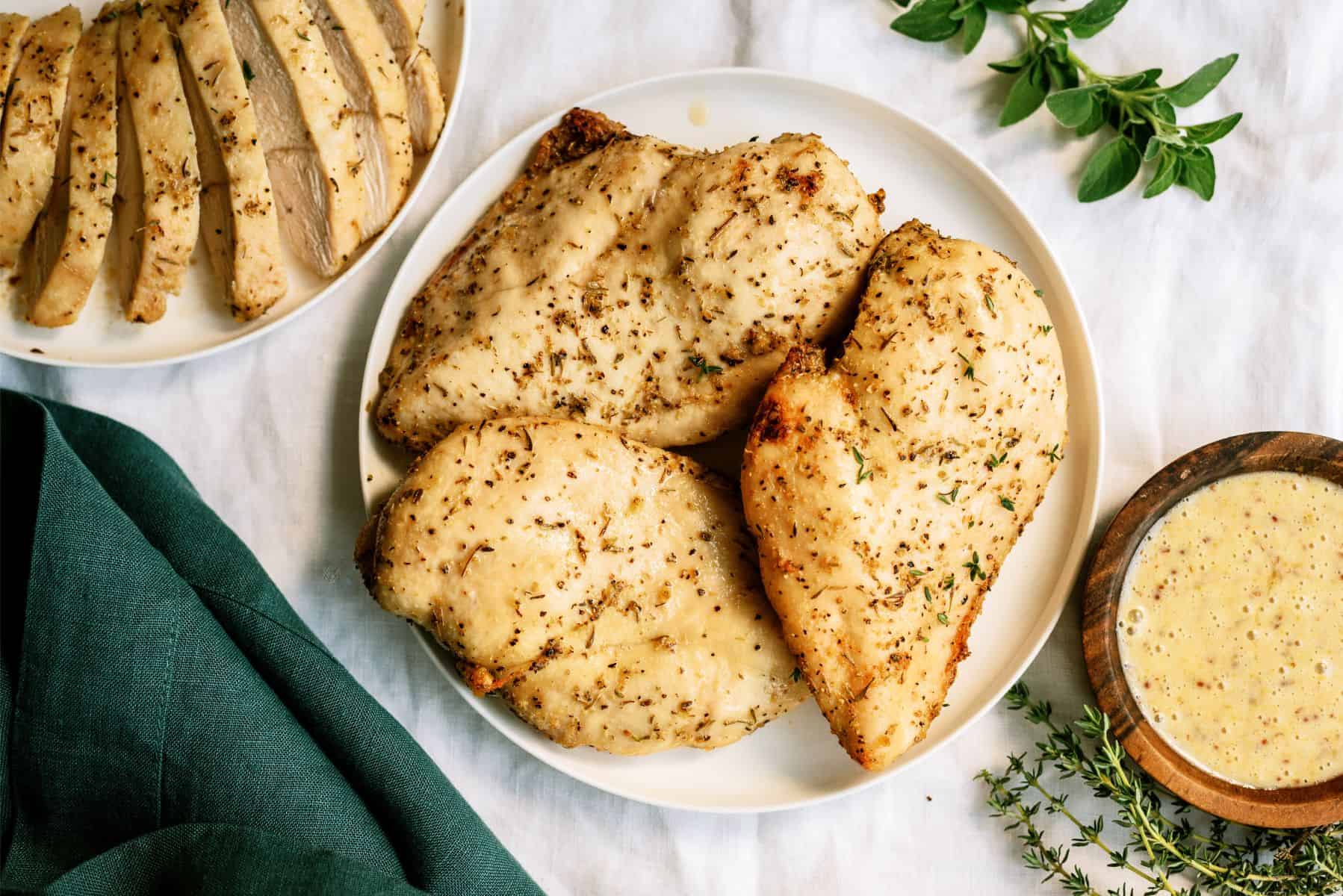 Baked Chicken Breast on a serving plate with sauce and more Baked Chicken Breast sliced on the side