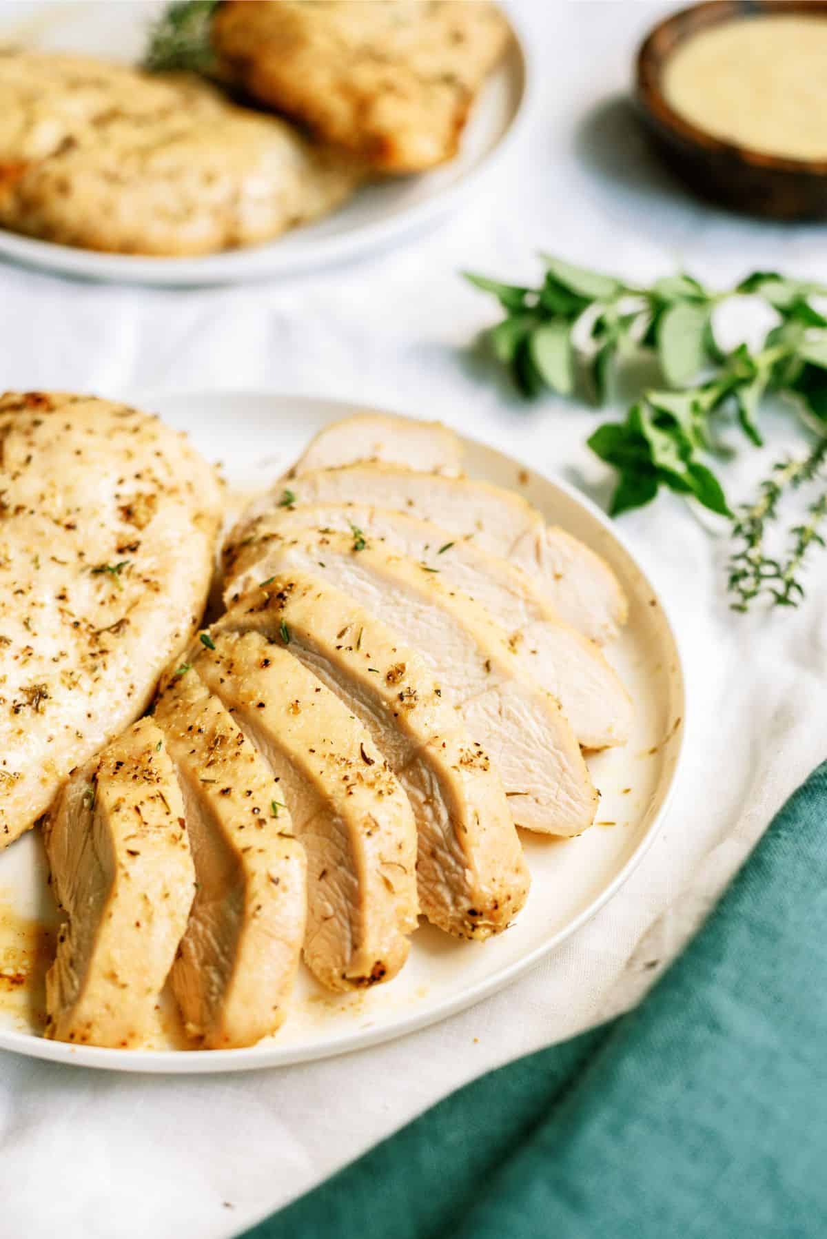 Sliced Baked Chicken Breast on a plate with another chicken breast behind it. A couple chicken breasts on a plate in the background.