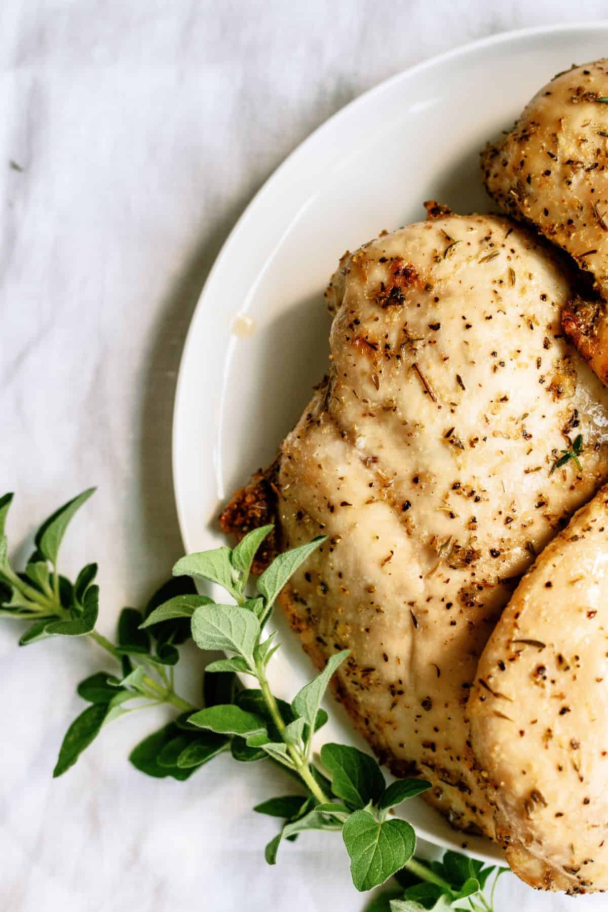 Baked Chicken Breast on a plate with herbs on the side.