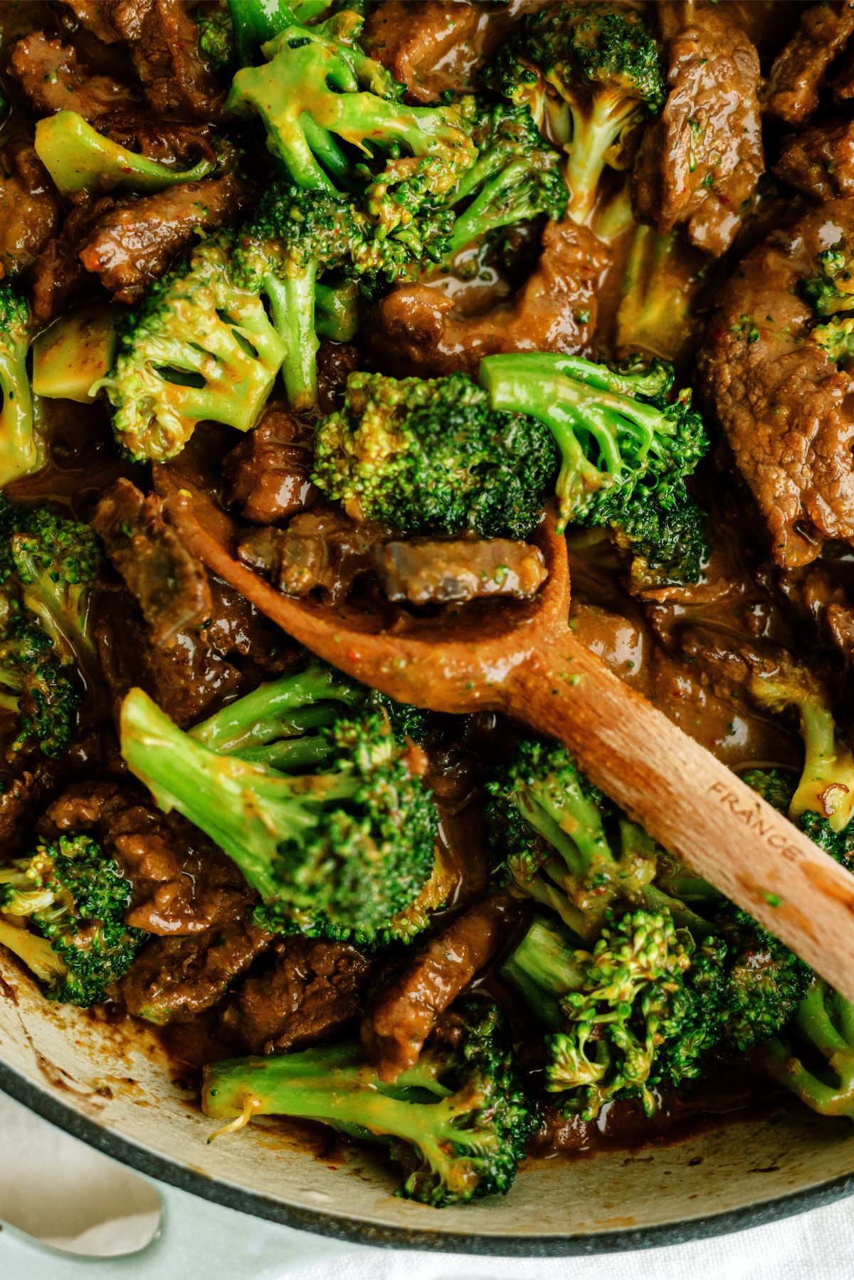 Close up of Beef and Broccoli Recipe in the skillet with a wooden spoon