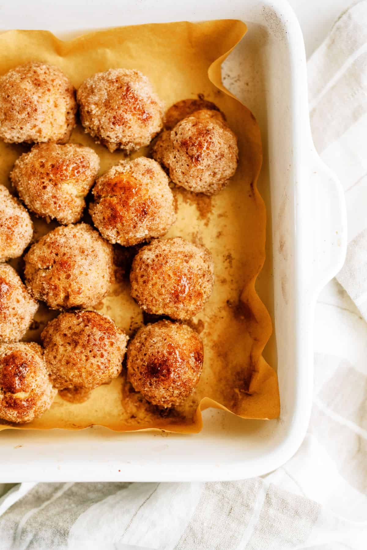 A baking dish filled lined with parchment pepper filled with baked Cinnamon Breakfast Bites dough balls.